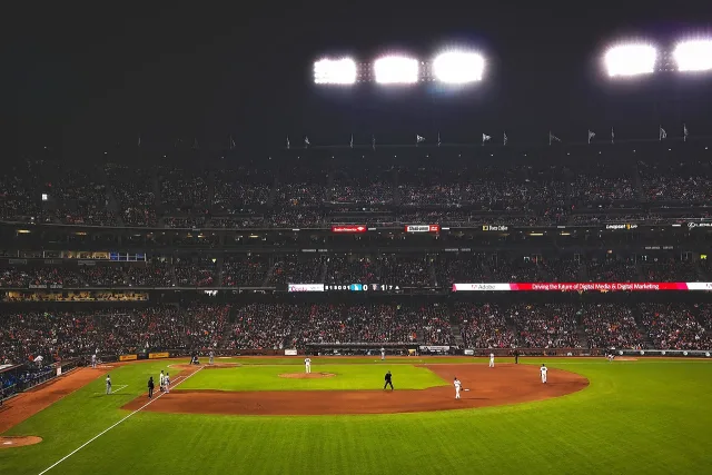A brightly lit cricket stadium at night during a match.
