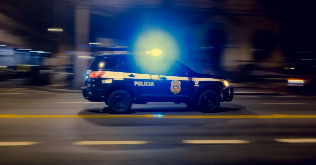 Blurred motion capture of a police car speeding at night with flashing lights on a city street.