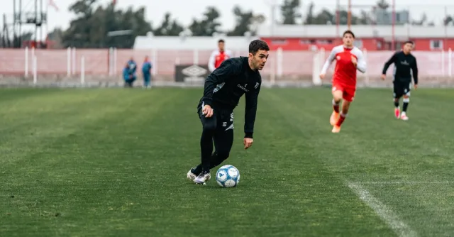 A soccer player dribbles on a green field during an intense match with teammates in pursuit.