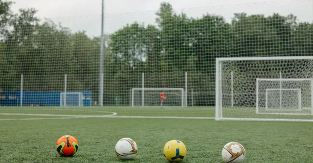 Four soccer balls on an outdoor field near goalposts, ideal for sports themes.