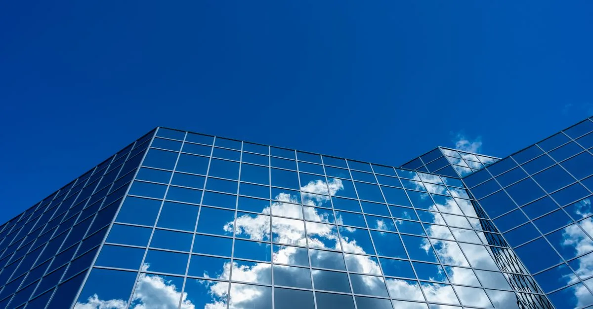 A modern skyscraper reflecting clouds against a vibrant blue sky.