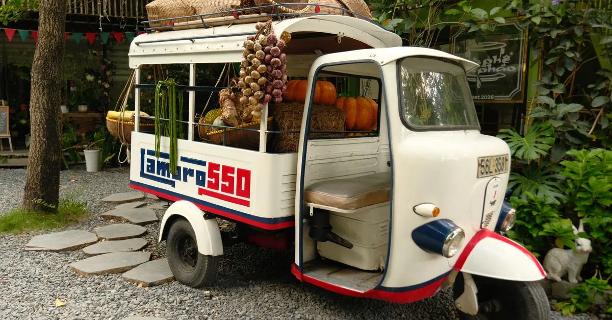 A vintage tuk-tuk carrying a variety of fresh produce like pumpkins and garlic, parked outdoors.