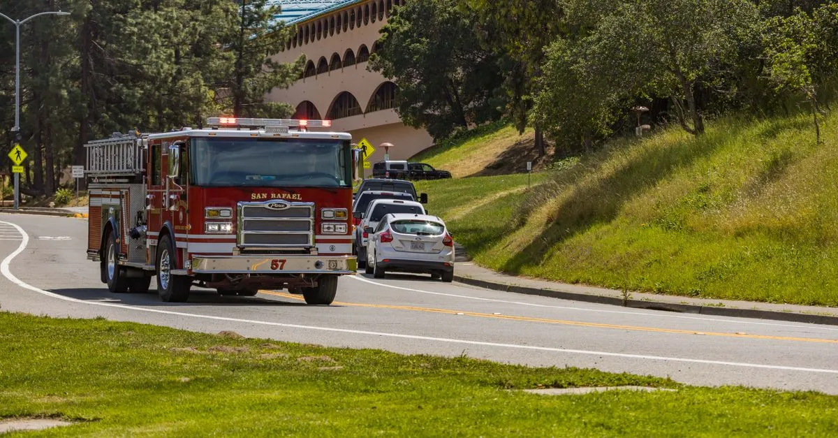A San Rafael fire truck driving along a sunny road with green surroundings in California.