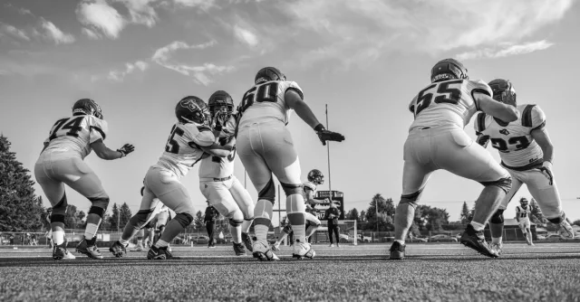 Black and white photo capturing a high school football game with players in motion on the field.