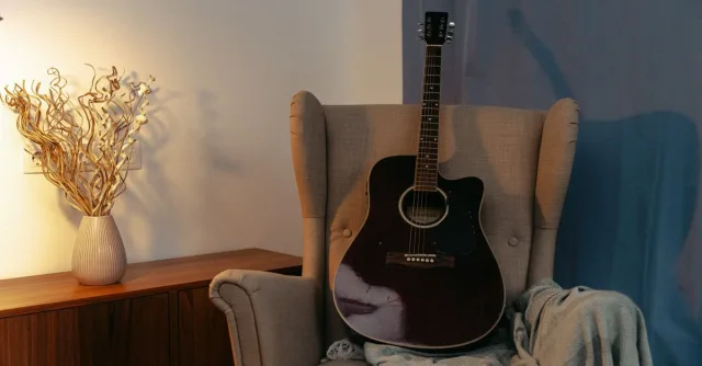 An acoustic guitar placed on a cozy armchair in a warm-lit living room setting.