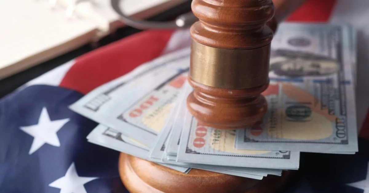 Close-up of a judge's gavel resting on US dollar bills and an American flag, symbolizing justice and finance.
