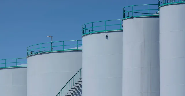 Large industrial storage tanks with green railings against a clear blue sky.