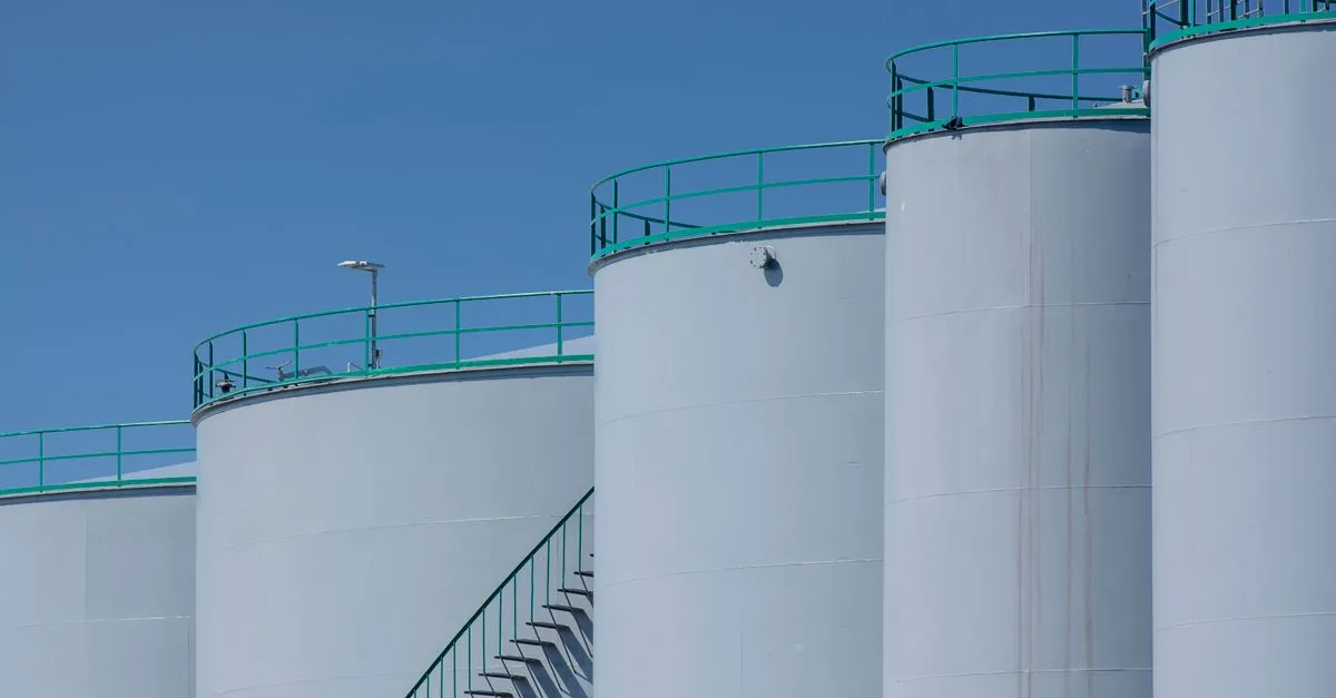 Large industrial storage tanks with green railings against a clear blue sky.