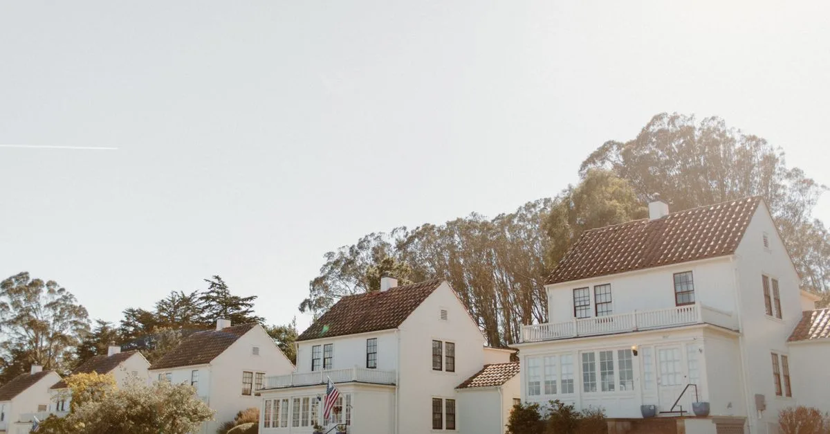 Sunlit view of classic white row houses in a green San Francisco neighborhood.