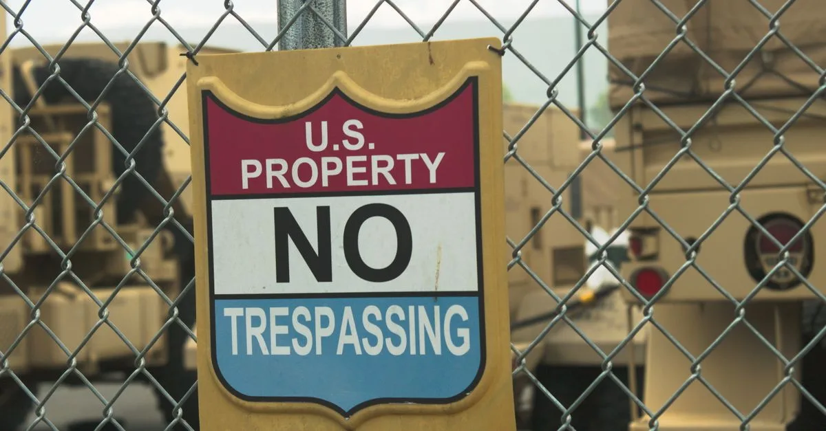 A no trespassing sign on a chain link fence at a U.S. property in Nevada with military vehicles in the background.