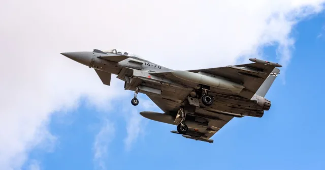 Eurofighter Typhoon aircraft landing with visible landing gear against a blue sky in Albacete, Spain.