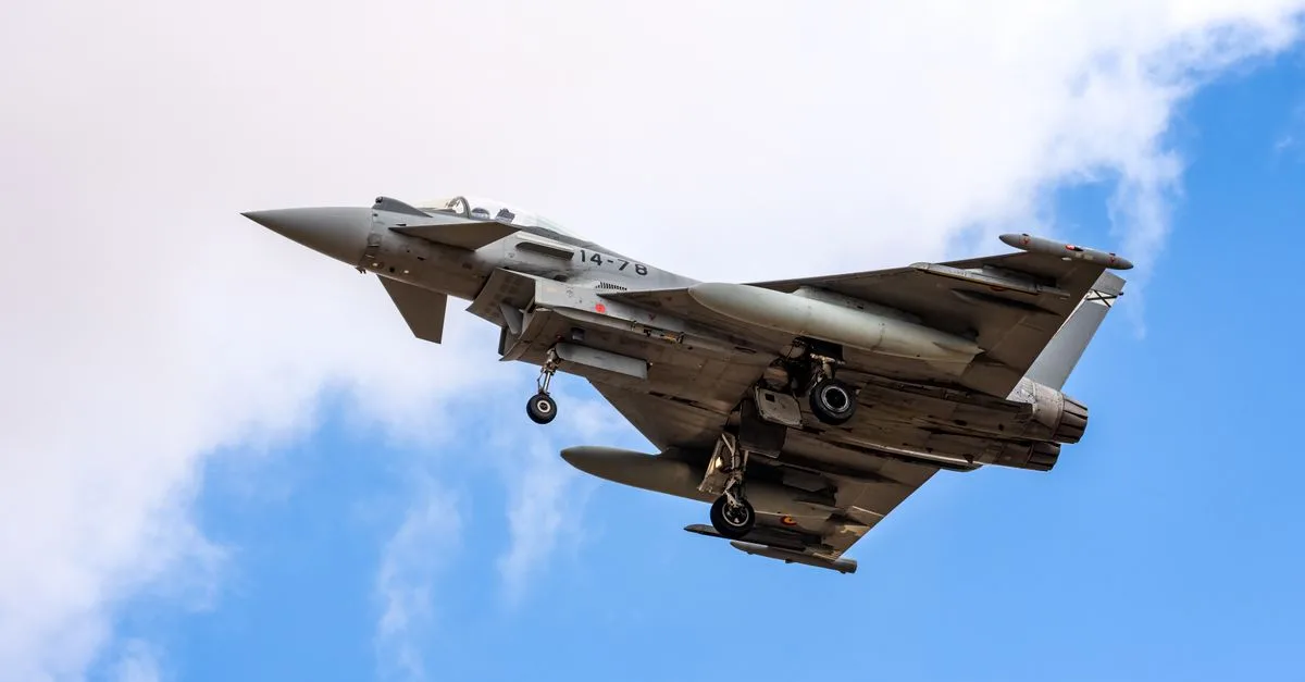 Eurofighter Typhoon aircraft landing with visible landing gear against a blue sky in Albacete, Spain.