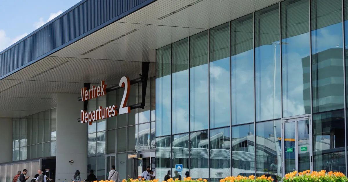 Glass facade of a bustling airport departure terminal with people outside and reflection of clouds.