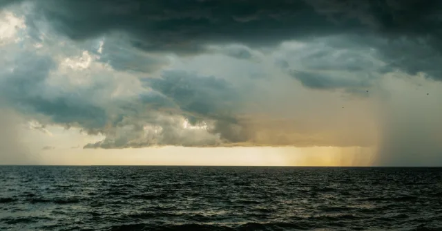 A vast ocean under stormy skies with dramatic dark clouds and rainfall.