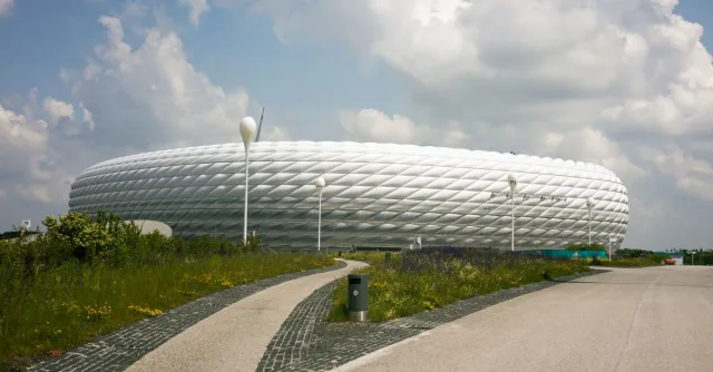 A striking modern stadium design under a cloudy summer sky, showcasing urban architectural beauty.