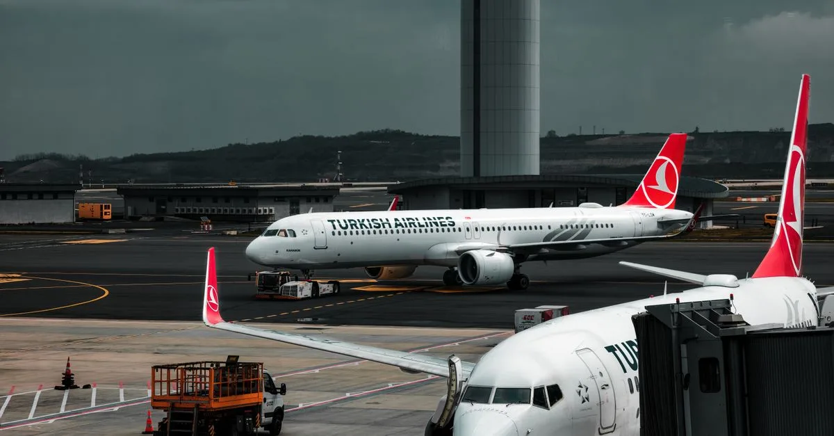 Turkish Airlines planes parked at an airport with a control tower in the background.