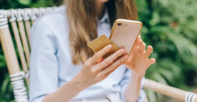 A woman making an online purchase using a smartphone and credit card outdoors.