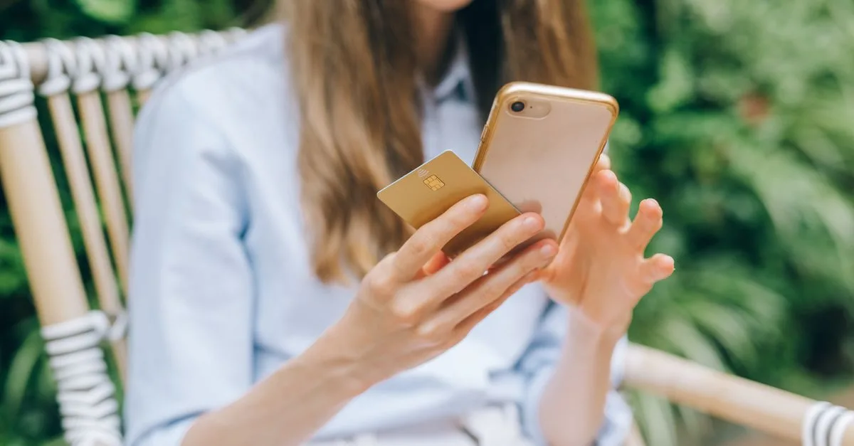 A woman making an online purchase using a smartphone and credit card outdoors.