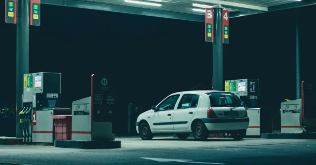 A solitary white car parked at a gas station under bright lights in a nighttime setting.