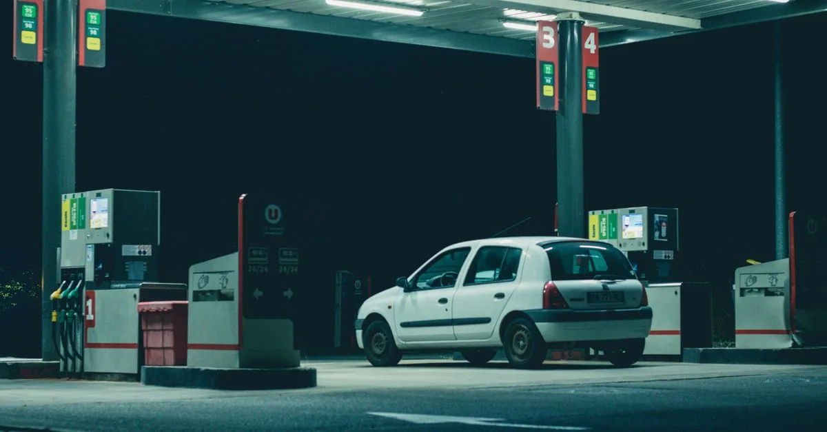 A solitary white car parked at a gas station under bright lights in a nighttime setting.
