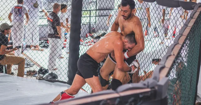 Two male MMA fighters engaging in an intense training session inside a gym cage.