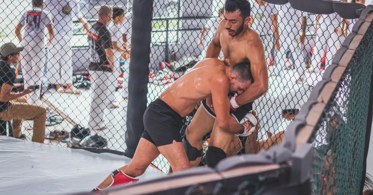 Two male MMA fighters engaging in an intense training session inside a gym cage.