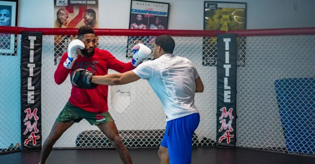 Two men engaged in an intense mixed martial arts training in an indoor gym.