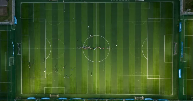 Top-down view of a soccer field with players during a daytime match.
