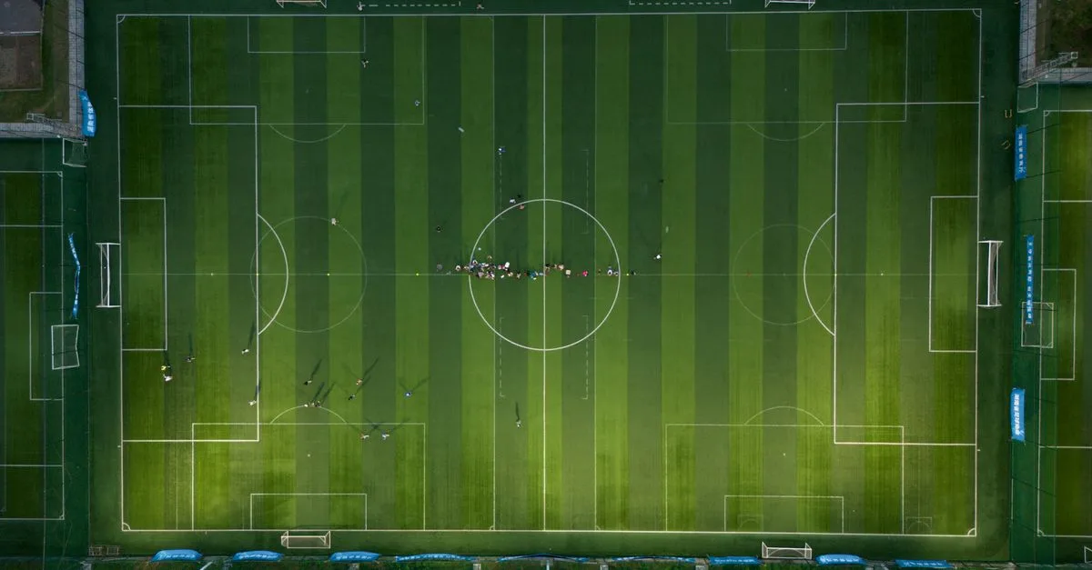 Top-down view of a soccer field with players during a daytime match.