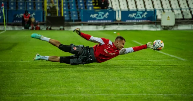 A soccer goalkeeper dives to make an impressive save during a match. Captured under stadium lights.