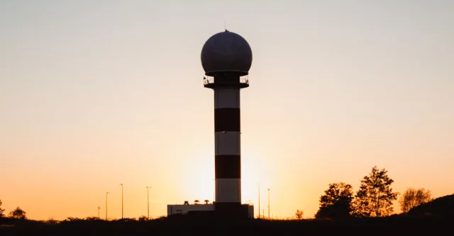 A radar tower silhouetted against a vibrant sunset with clear skies.