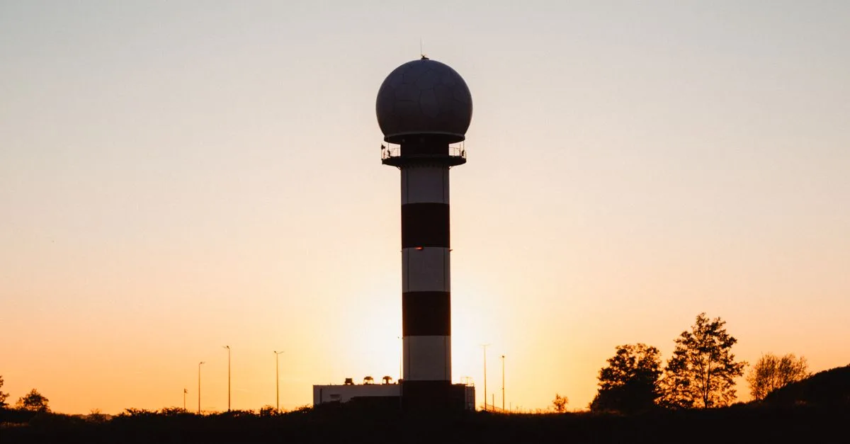 A radar tower silhouetted against a vibrant sunset with clear skies.