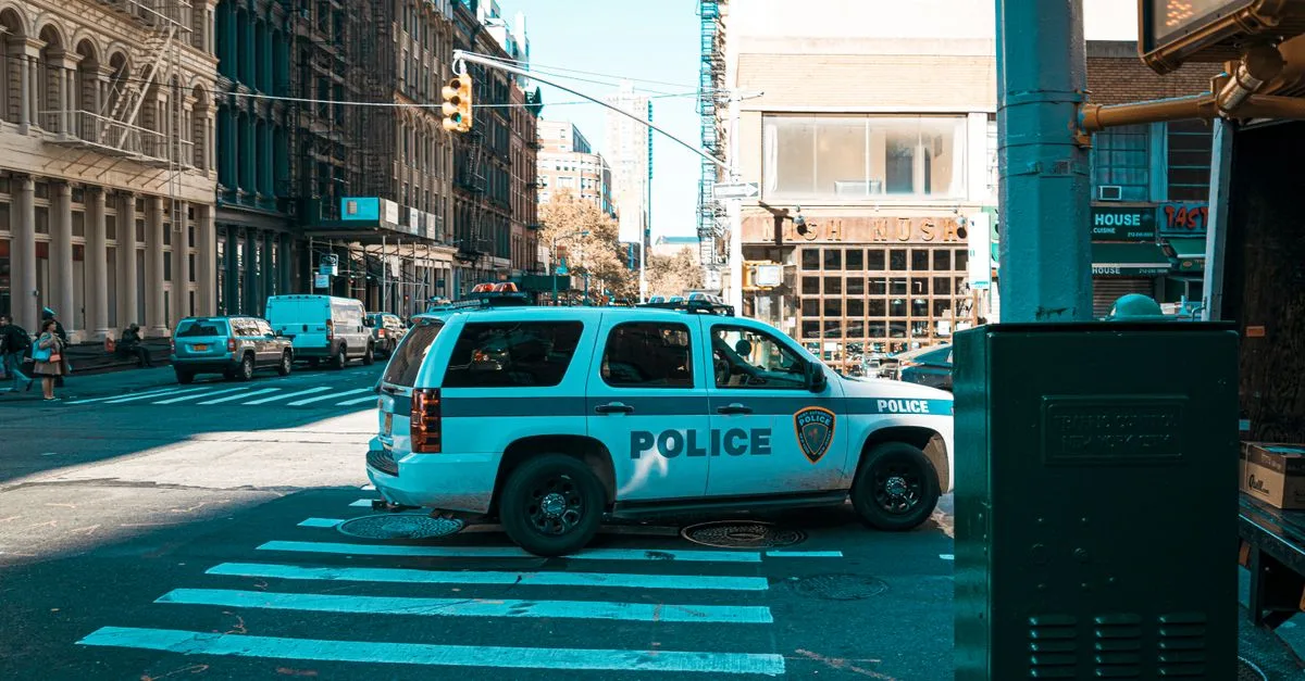 A police SUV at an urban intersection in New York City with pedestrians and traffic.