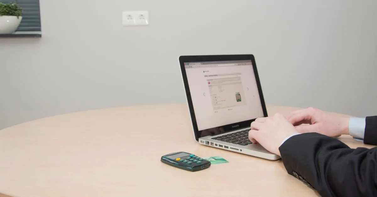 A professional working on a laptop at a round table with a card reader nearby.