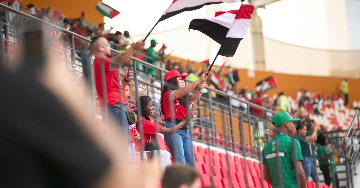 Soccer fans in the stadium wave Egyptian flags, showing their support during a lively sports match.