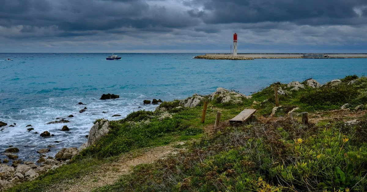 Stormy seascape featuring a lighthouse on a rocky coast, highlighting dramatic skies.