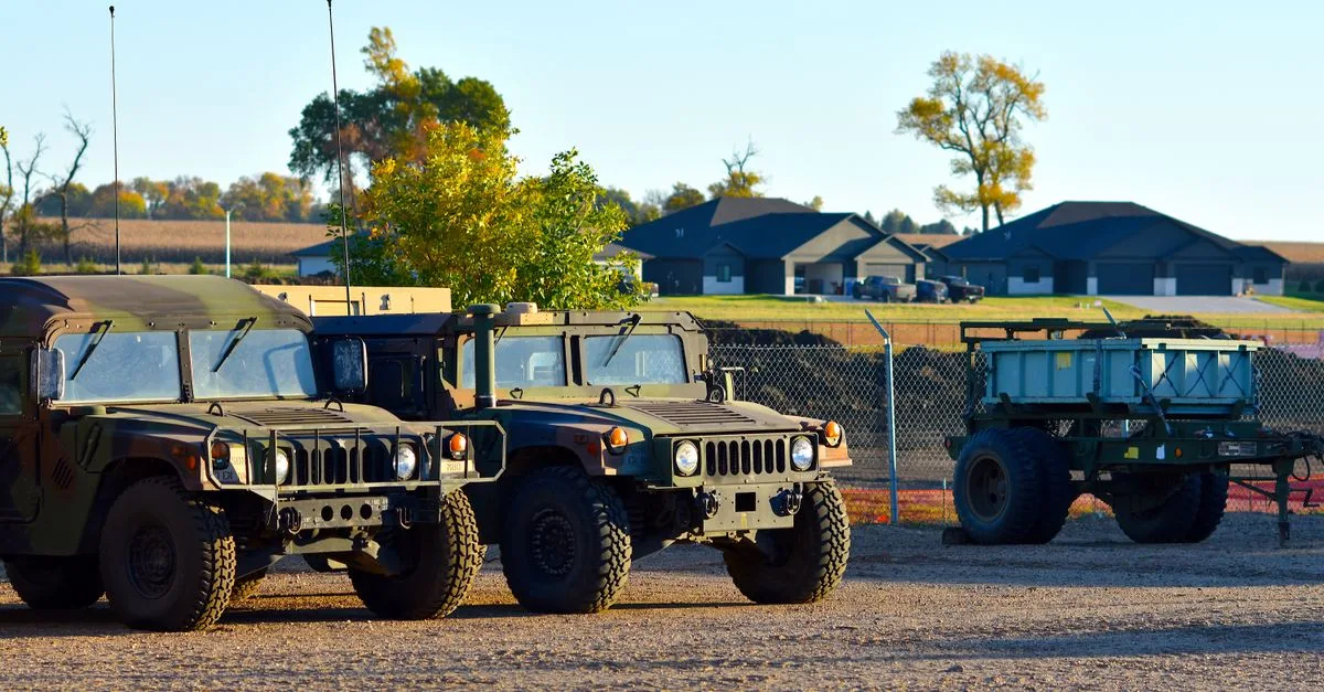 Military vehicles, including Humvees, parked outdoors near homes in autumn.