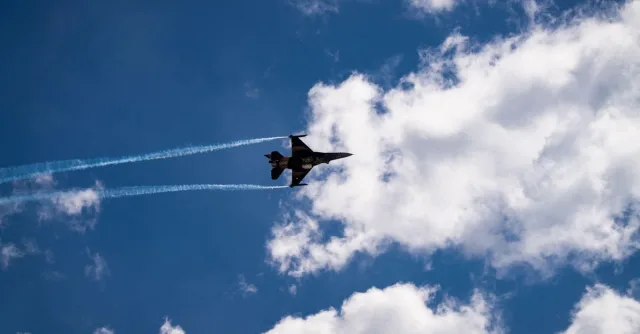 Silhouette of a fighter jet soaring through a vibrant blue sky with streaks of white clouds.