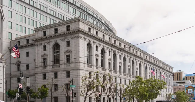 Elegant neoclassical courthouse in San Francisco with American flags outside.