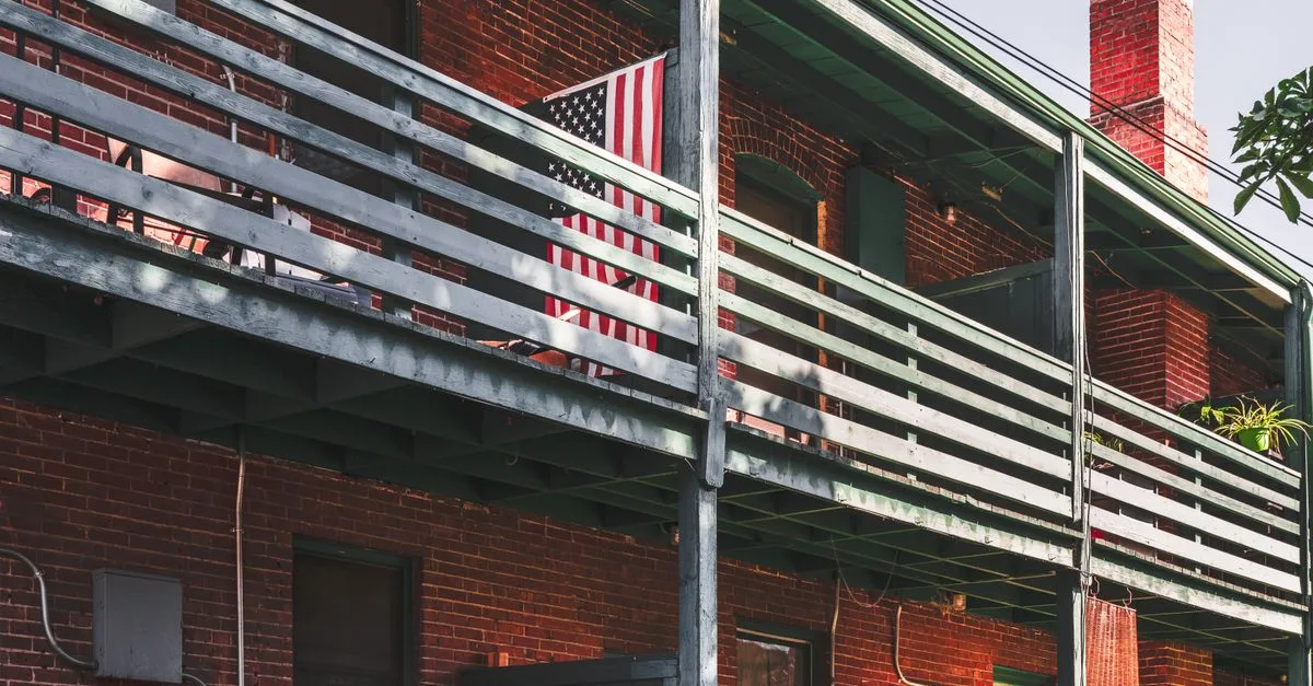 A rustic brick building featuring a prominently displayed American flag on its balcony.