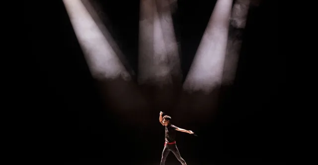 Energetic performance by male dancer under dramatic stage lighting.