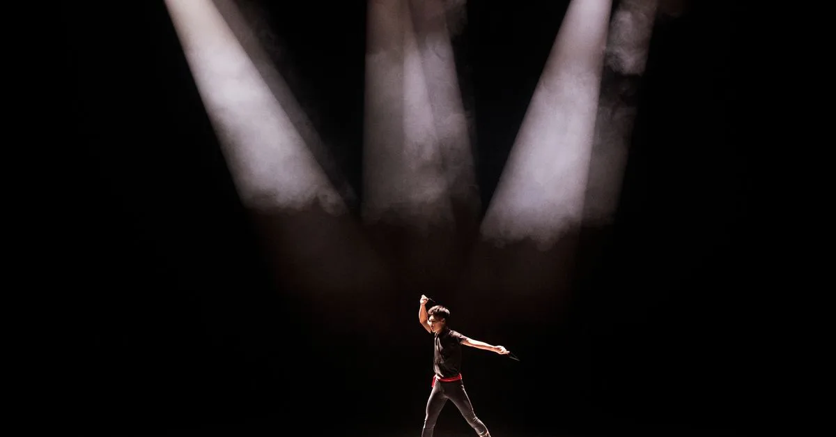 Energetic performance by male dancer under dramatic stage lighting.
