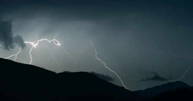 Captivating shot of lightning illuminating a dark sky over mountain silhouettes during a thunderstorm.