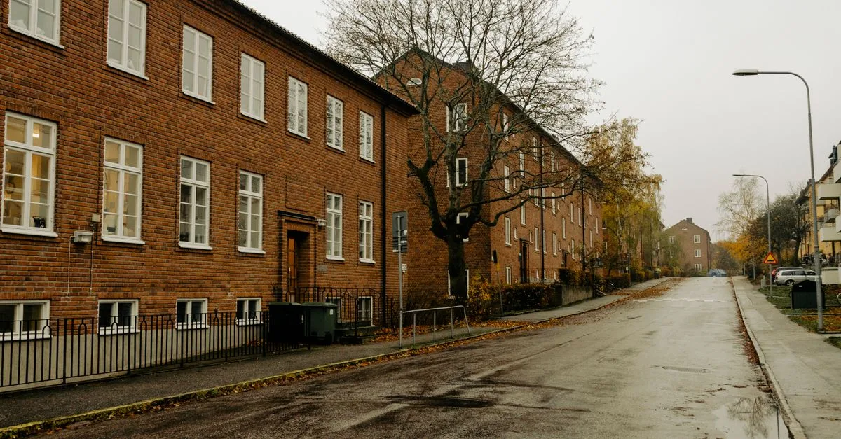 A quiet, wet residential street in Stockholm with brick buildings and autumn foliage.
