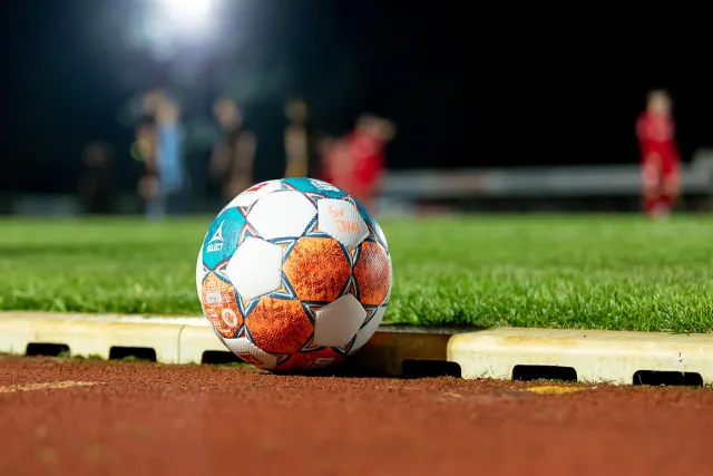 A wide view of an empty soccer stadium pitch under bright daylight.
