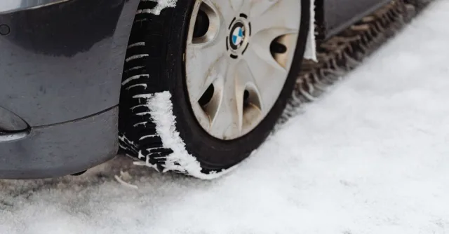 Close-up of a car's tire on a snowy road, highlighting the winter season conditions.