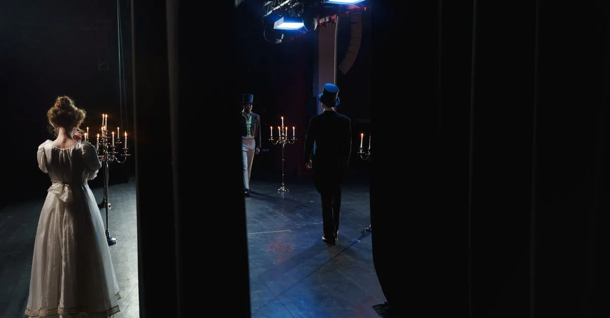 A captivating backstage view of actors in vintage costumes performing on a dimly lit theater stage.