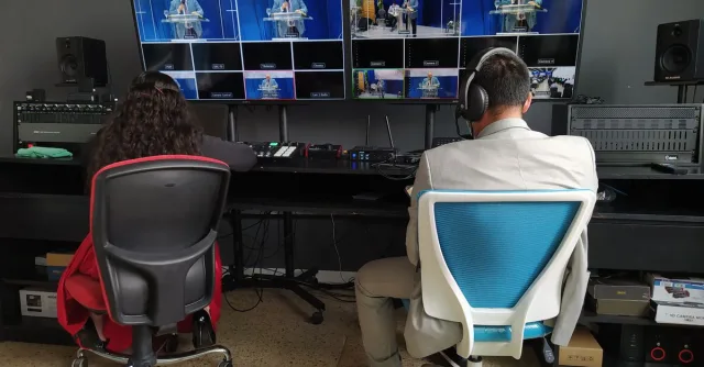 Back view of broadcast editors working at panel with equipment and big monitors