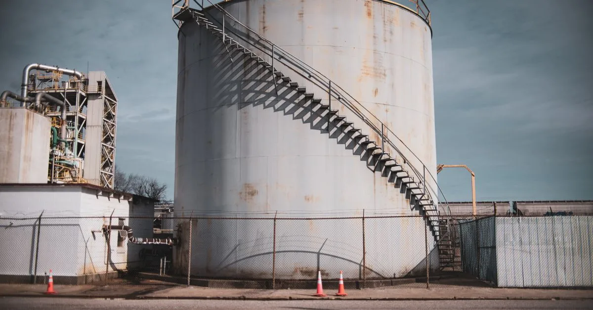 Industrial storage tank with metal stairs in an outdoor facility under clear sky.