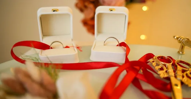 Stylish wedding rings in velvet boxes alongside decorative scissors and red ribbon on a festive table.